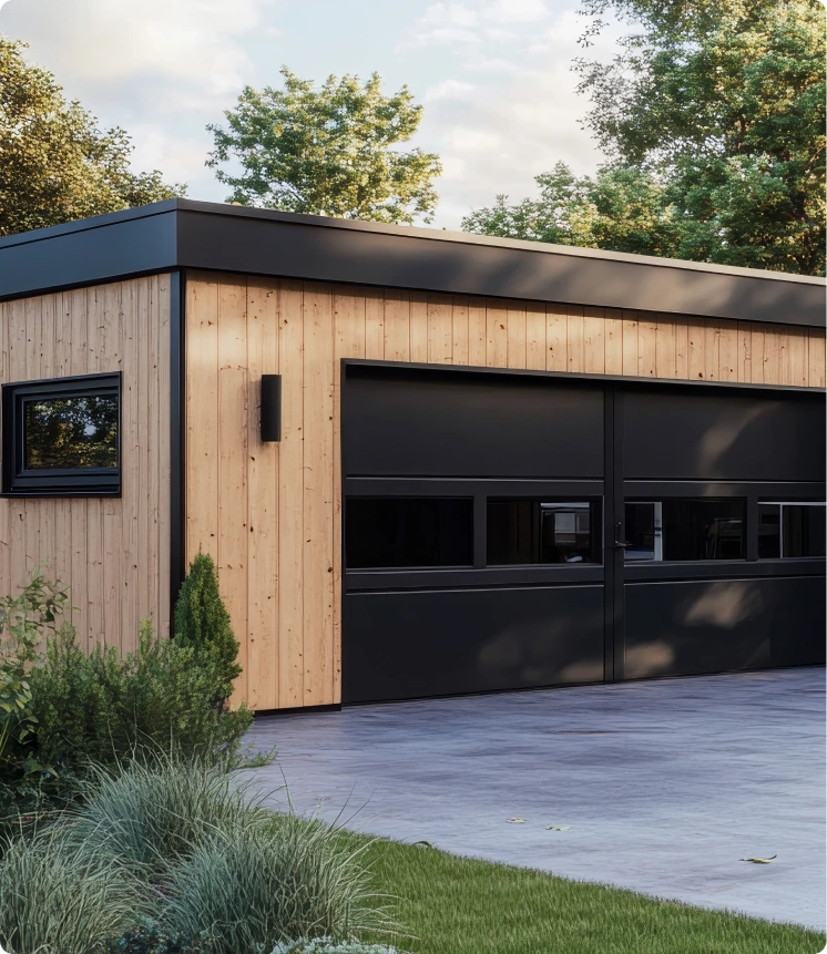 Modern garage with flat roof, vertical wooden paneling exterior, black-framed rectangular window and large double garage door with horizontal windows, surrounded by paved driveway, landscaped grass and shrubs, with tall trees in background under partly cloudy sky.